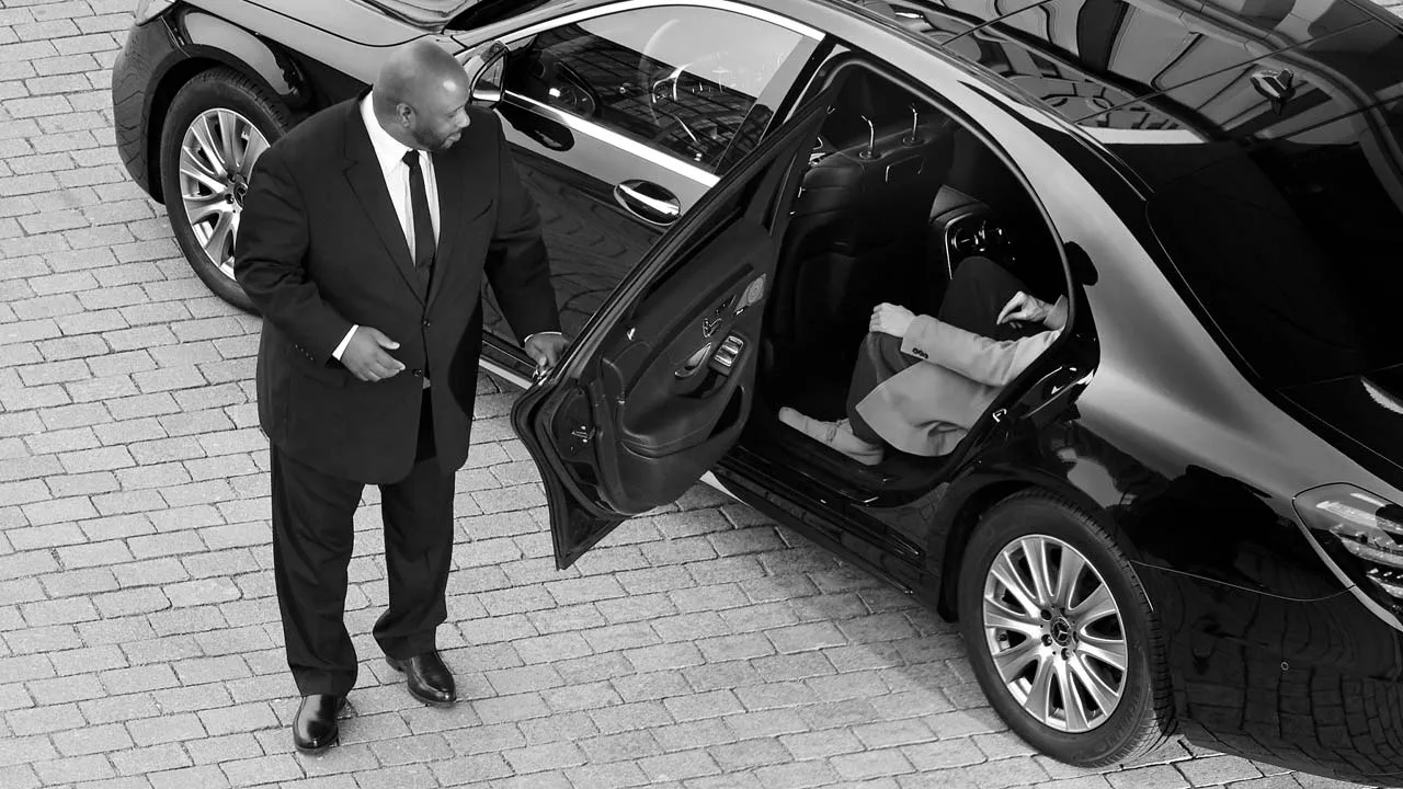 Professional driver in suit standing by town car